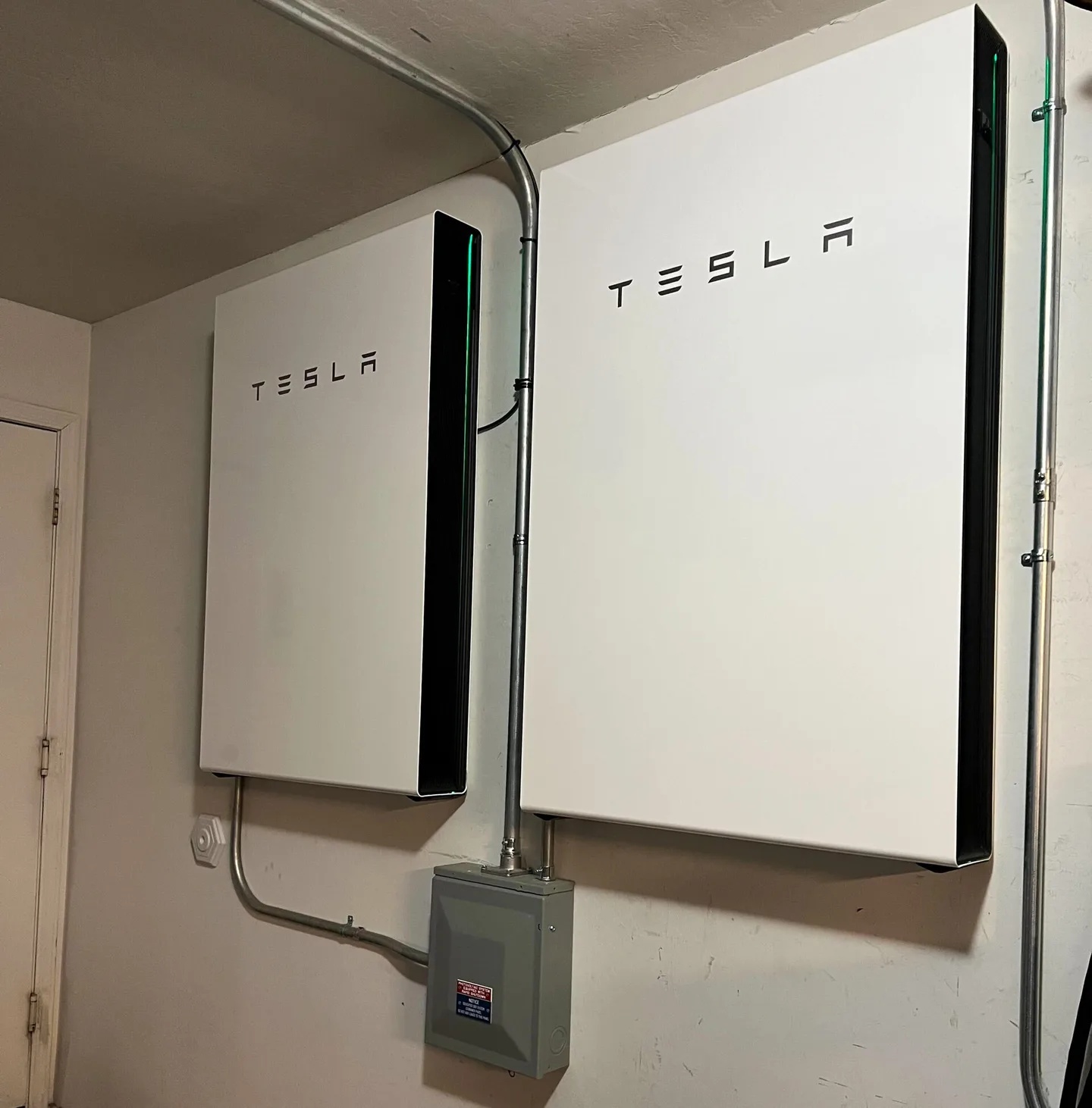 Twee witte muurbatterijen (Tesla Powerwall 3) aan een muur met leidingwerk en schakelkast